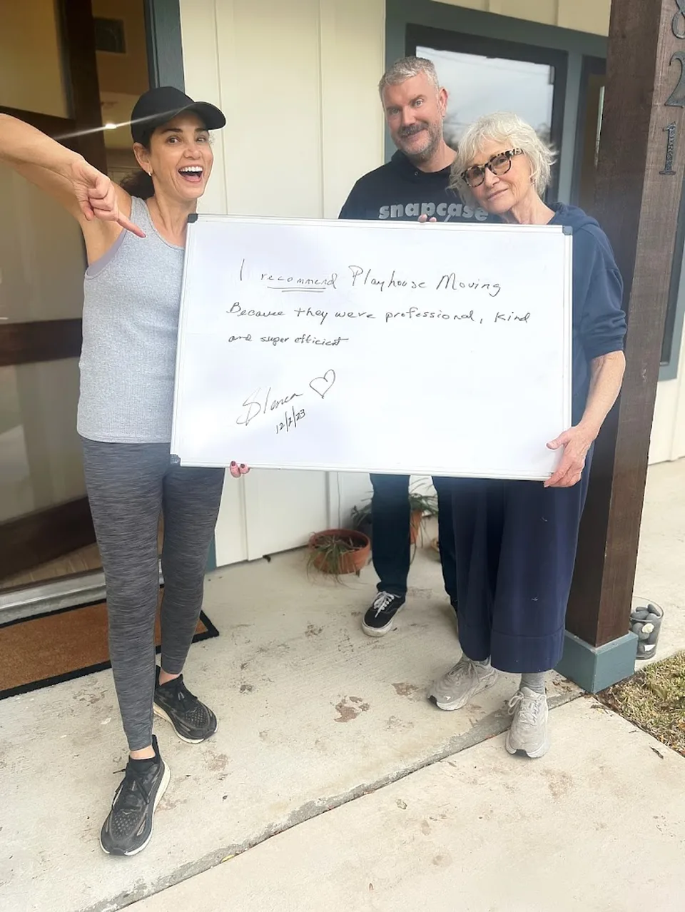 Three happy customers with a recommendation board describing Playhouse Moving as professional, kind and super efficient