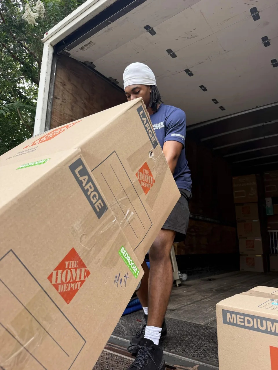 Playhouse Moving crew member carrying a large moving box out of a truck