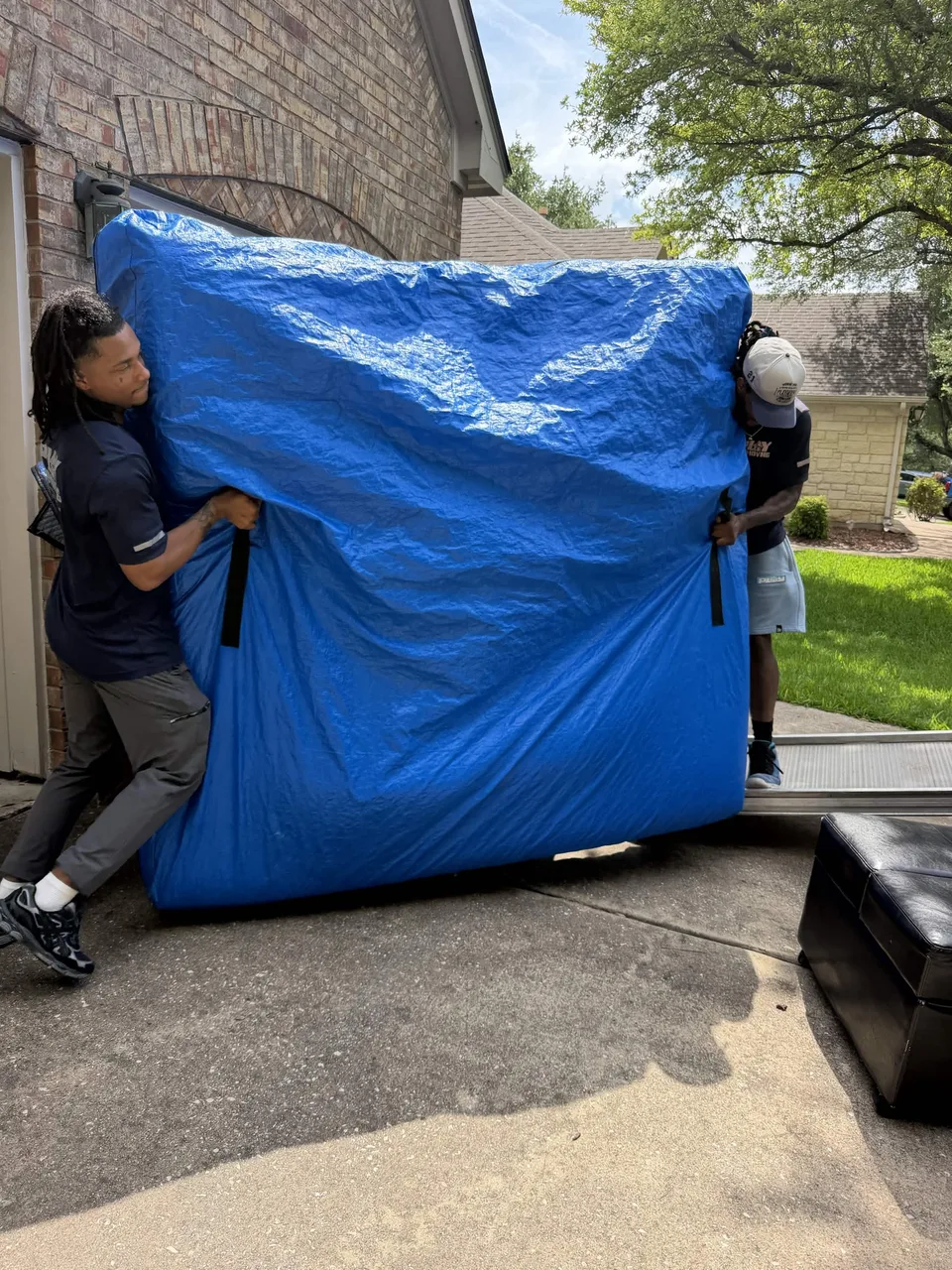 Two crew members carrying a large covered mattress out of a home