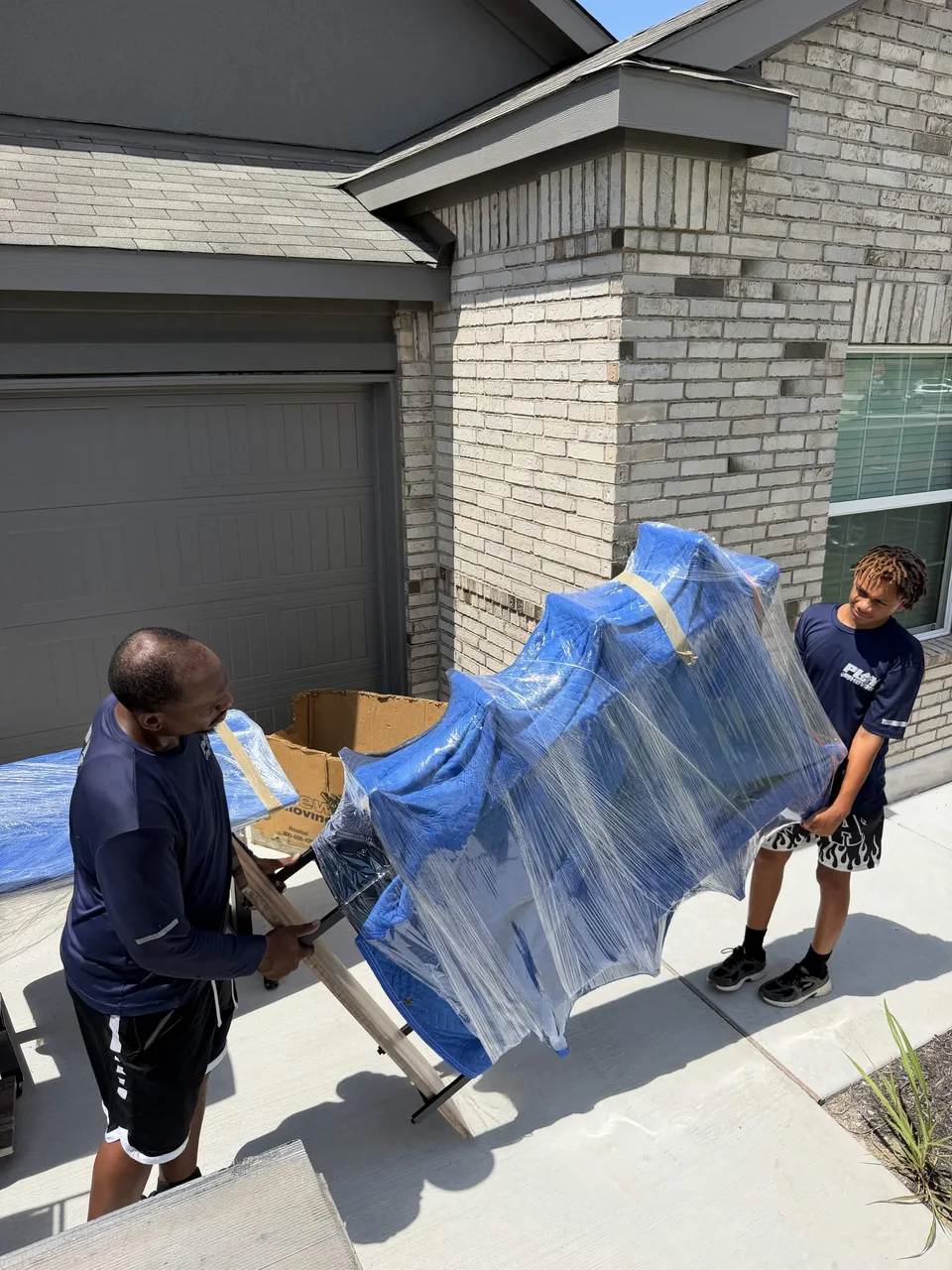 Two crew members bringing wrapped furniture toward a moving truck ramp