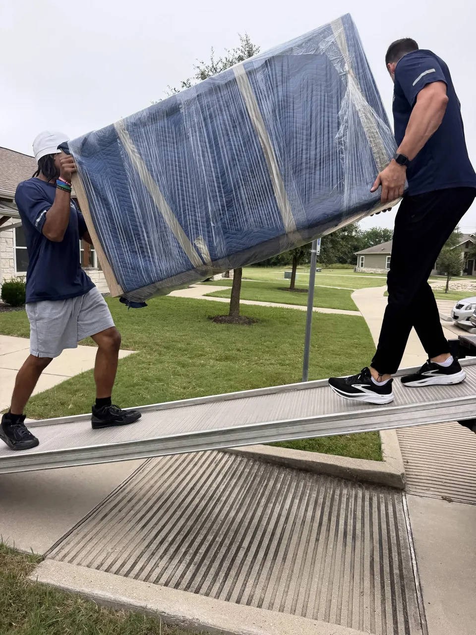 Two Playhouse Moving crew members carrying wrapped furniture up a truck ramp