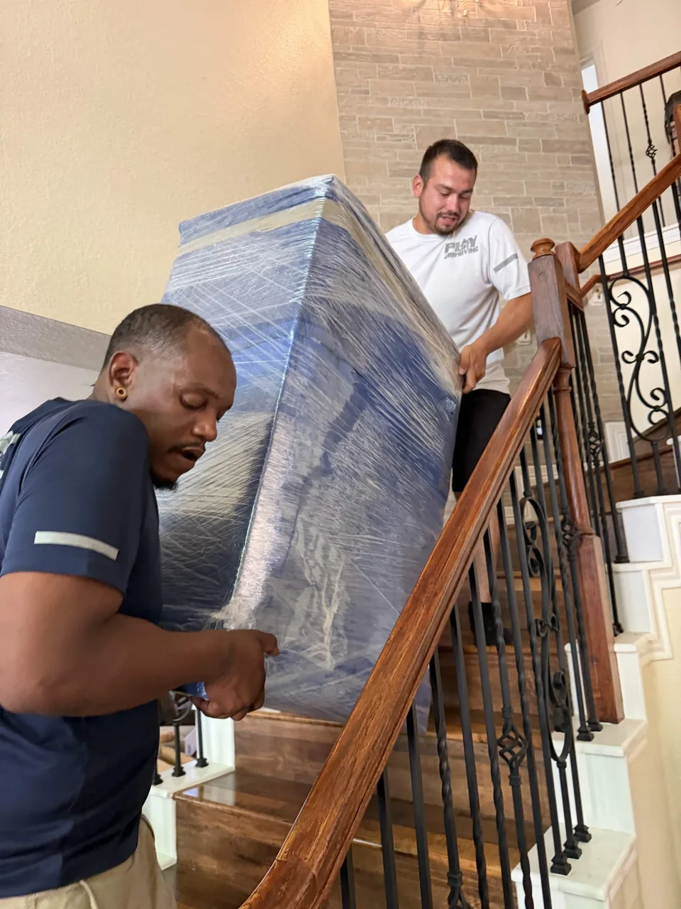 Two crew members carefully carrying wrapped furniture down a curved staircase