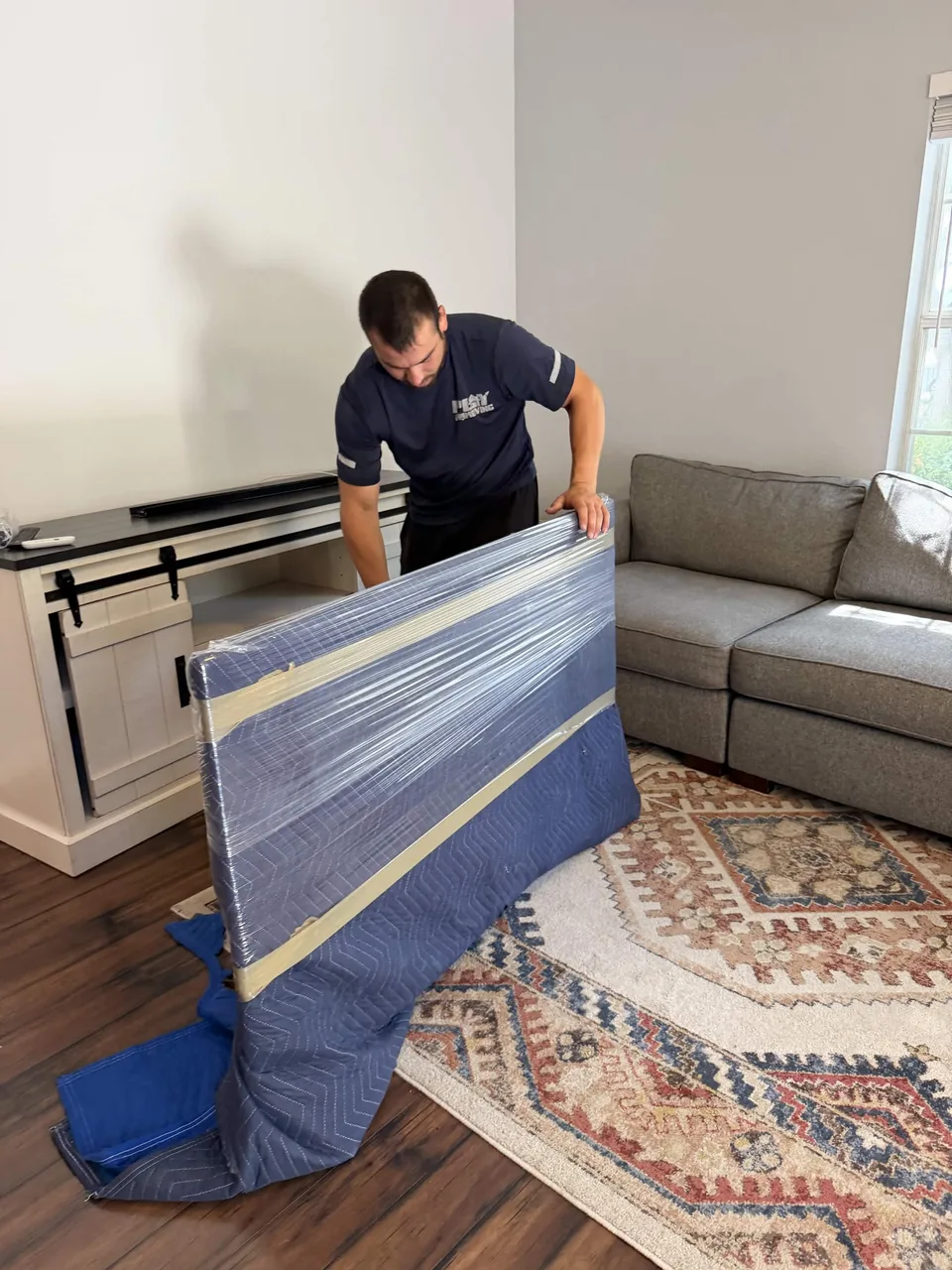 Crew member securing a furniture panel with a moving blanket and stretch wrap
