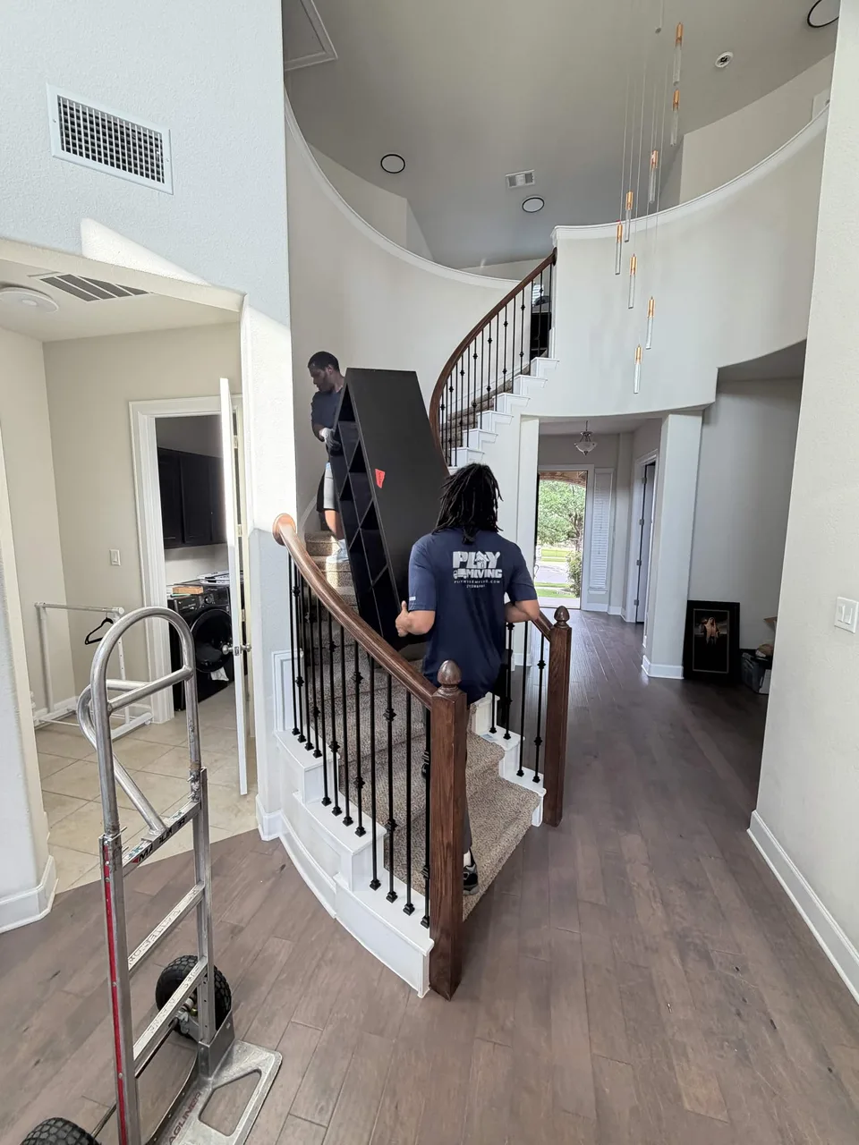Two Playhouse Moving crew members carrying a shelving unit on a curved staircase inside a home