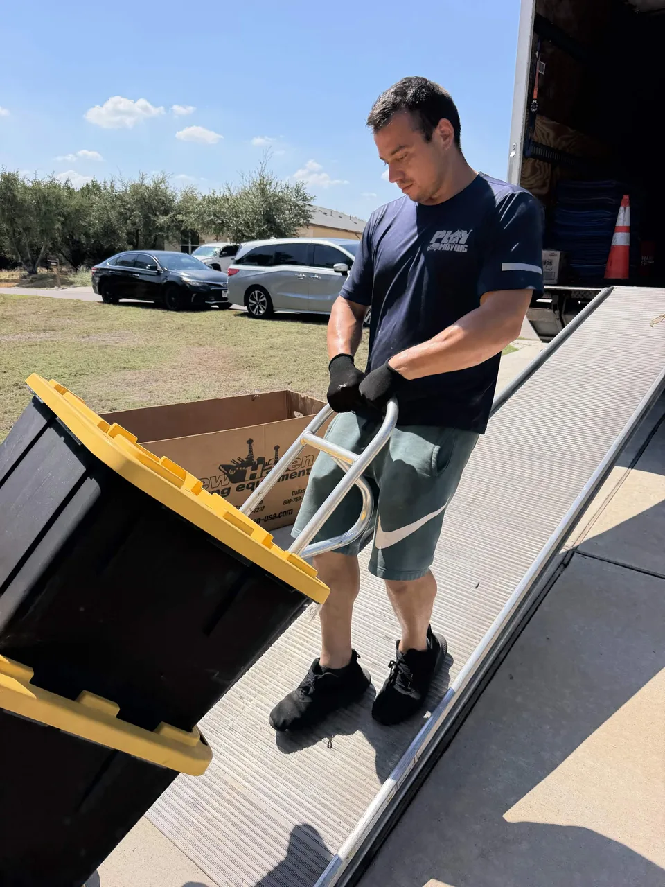 Playhouse Moving crew member moving storage bins on a hand truck along a loading ramp
