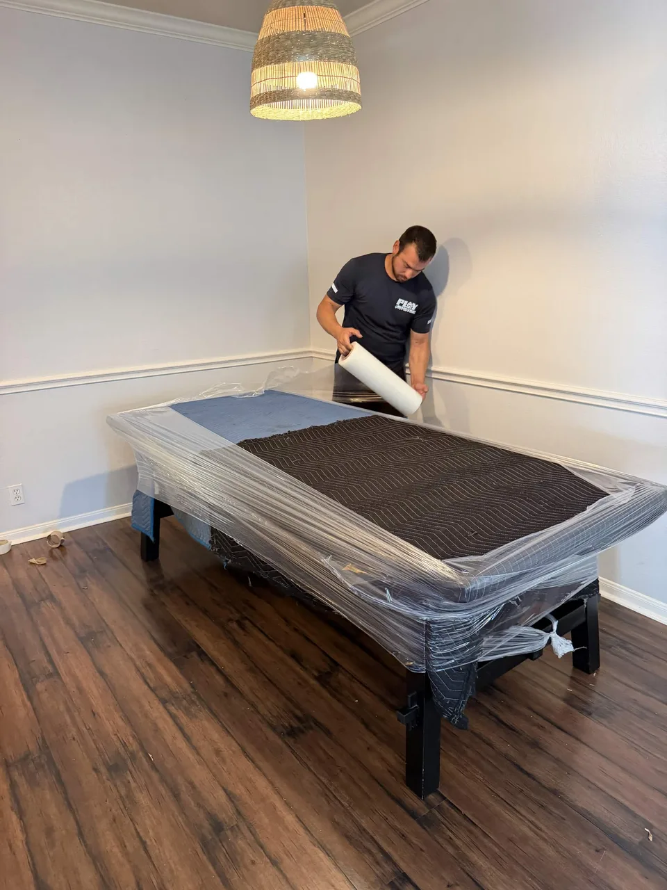 Playhouse Moving crew member wrapping a dining table with moving blankets and stretch wrap